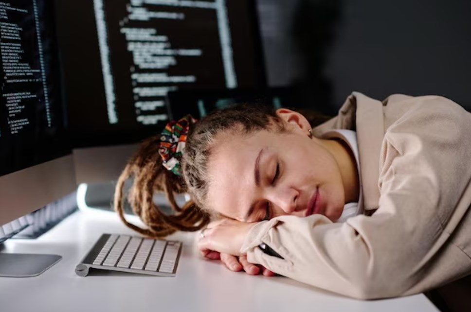 a young female IT engineer sleeping in front of her PC screen with her head on the desk