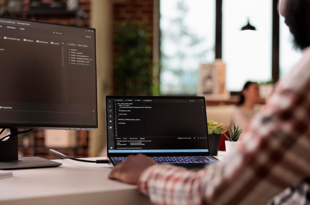 man in shirt typing on a laptop with the coding on it, the computer screen on the left side with coding