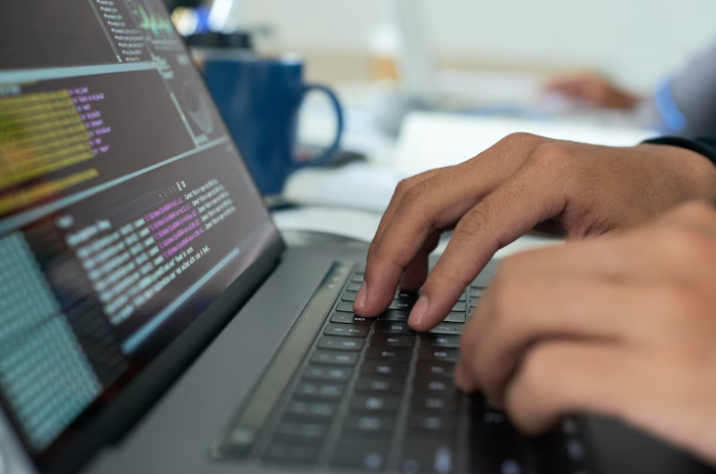 hands typing on a laptop keyboard, the screen with the coding on it, blue cup and sheets on blurred background