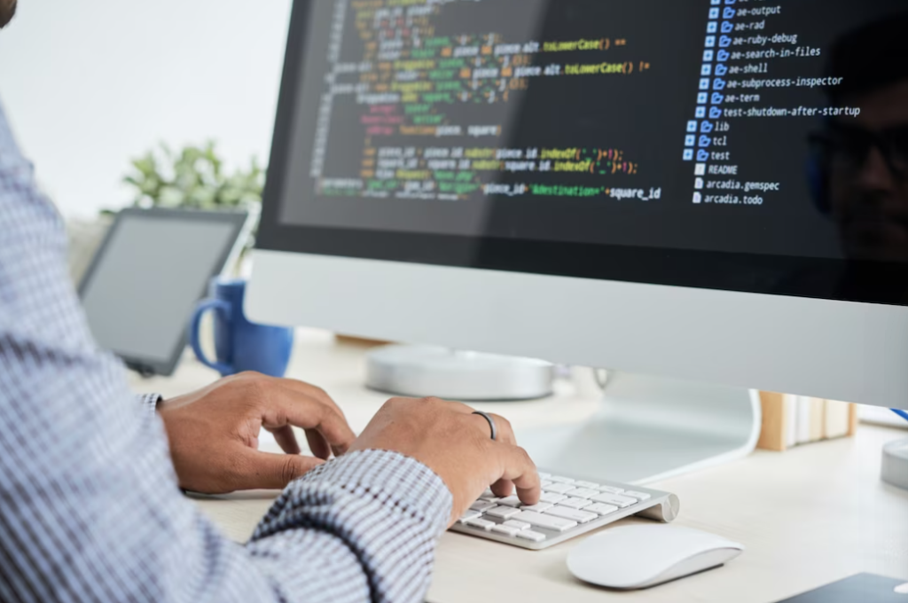 person in a shirt sitting at the table and typing on the keyboard, the screen with coding on it