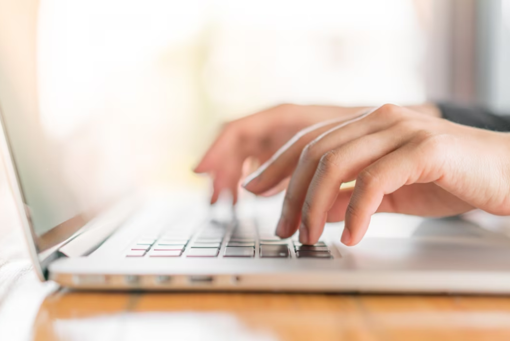  a side view of hands typing on a laptop keyboard