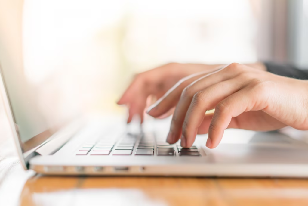 a side view of hands typing on a laptop keyboard